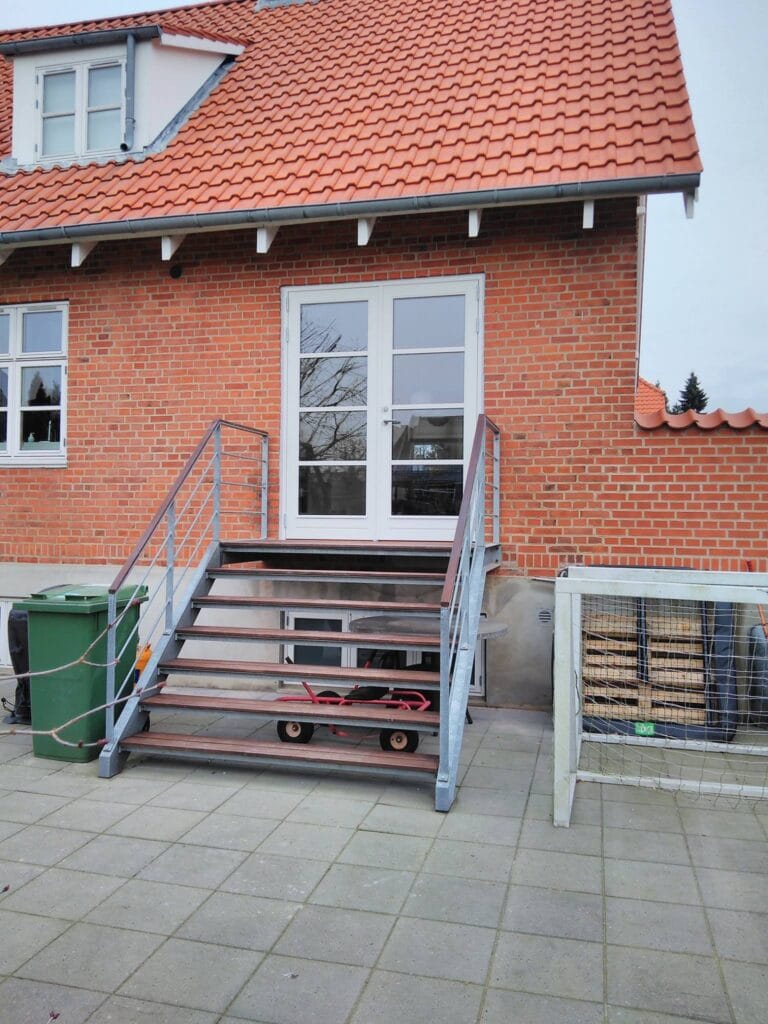Murstenshus med trappe og rødt tegltag